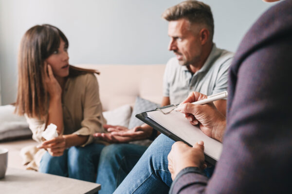 Photo of angry irritated couple man and woman having conversation with psychologist on therapy session in room