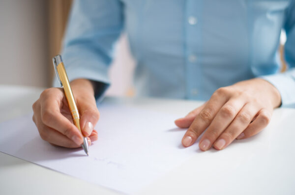 Closeup of woman writing on sheet of paper. Paper sheet lying on desk. Application concept. Cropped front view.