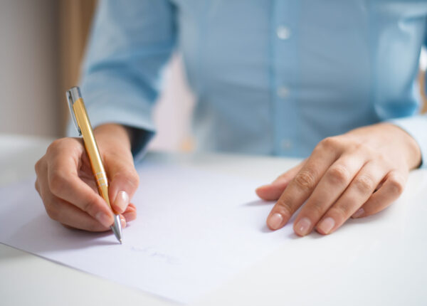 Closeup of woman writing on sheet of paper. Paper sheet lying on desk. Application concept. Cropped front view.