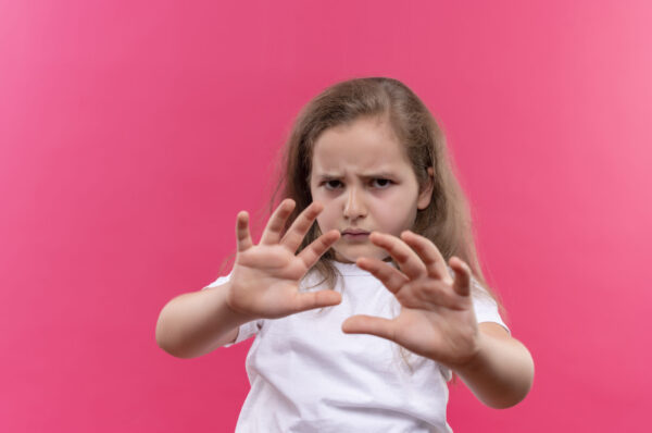 sad little school girl wearing white t-shirt showing stop gesture on isolated pink background