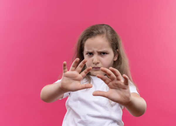 sad little school girl wearing white t-shirt showing stop gesture on isolated pink background