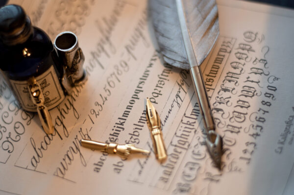 A macro shot of a quill set and an ink bottle on a piece of paper with calligraphy on it
