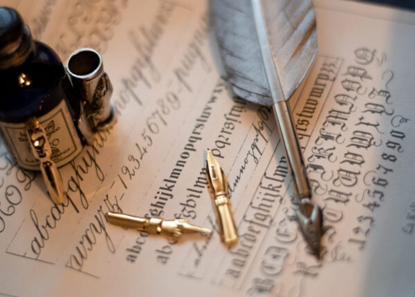 A macro shot of a quill set and an ink bottle on a piece of paper with calligraphy on it
